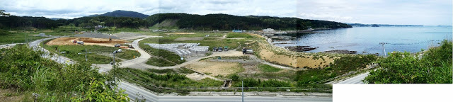 広く造成された土地に中央に道が曲がりながら走っており、ところどころに重機が置かれ右側には海が広がっている旧戸倉中学校から写したパノラマ写真