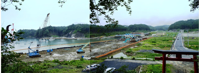 鳥居の前に道路が通り左側の海岸には大きなクレーン車や重機も多数稼働している復旧作業中の写真