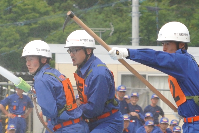 ヘルメットと番号付きのビブスを着た消防団員3人が放水操作をしている訓練中の写真