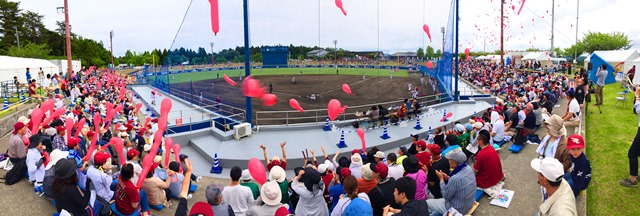 観客席で多くの人々が応援しながら、赤い風船を一斉に飛ばし、盛り上がっている様子を写した写真