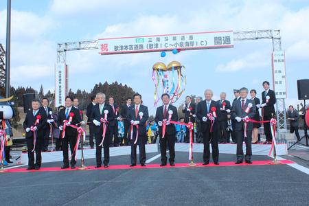 7人のスーツ姿の男性が横一列に並び、三陸道開通式にてテープカットを行った写真