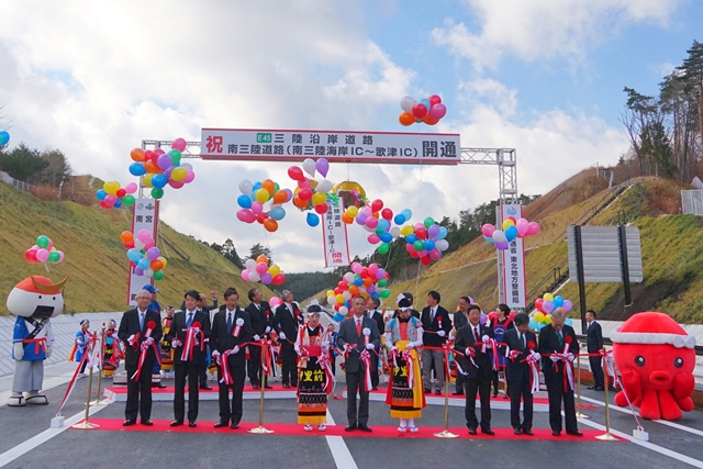 色とりどりの風船が舞う中、スーツ姿の関係者や郷土衣装を着た子どもたちが並び、テープカットで新しい高速道路の開通を祝う式典が行われている写真
