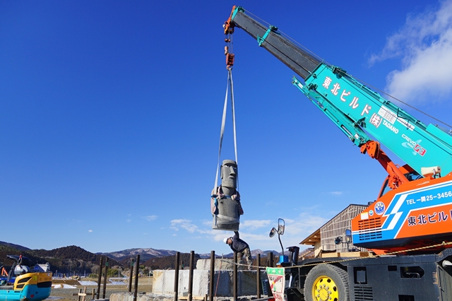クレーン車で大きなモアイ像を慎重に吊り上げて移動させている写真