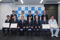 前列の中央に座っている3名の男性、両脇に2名ずつ賞状を持って座っている男性、後列に5名の男性が立ち記念撮影をしている写真