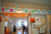 「子育て支援センター」の入口にハロウィンの装飾が施され、オレンジのガーランドや笑顔のオバケ飾りが掲げられた賑やかな雰囲気の室内イベント会場を写した写真