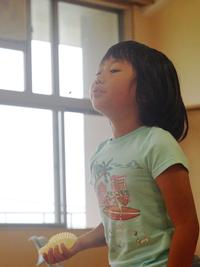 水色の服を着た女の子が、口をとがらせてスイカの種を飛ばそうとしている様子の写真