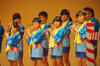 色鮮やかな青と黄色の法被を着た子どもたちが並んで立ち、それぞれが真剣な表情で笛を吹いている演奏風景の写真