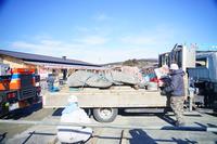 横になったモアイ像がトラックに積まれ、作業員が荷台の周りで作業している様子を写した写真