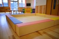 子供用の遊び場に設けられた、赤・青・黄・緑などのカラフルなクッションで四方を囲まれた安全な四角いスペースが写されている写真