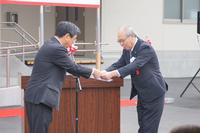 佐藤町長と、スーツを着た年配の男性が向かい合って立ち、紙のようなものの授受を行っている写真