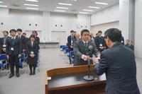 演台に立っている男性が、向かい側に立っている男性の紙を手渡している写真