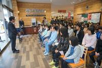 4列ほどに並べられた椅子に関係者の方々が座り、前方で立って話をしている市長の方を見ている写真