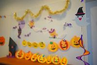 白い壁に沿って金色のモールや手作りのカボチャやオバケの飾りが多数並べられ、ハロウィンをテーマにした可愛らしい装飾が施された室内の一角を写した写真