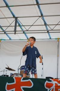 野外ステージの上で浴衣姿の男の子がマイクを持って歌っている写真