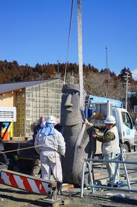 クレーンで吊り上げられたモアイ像を地面に立たせ、作業員が支えている様子を写した写真