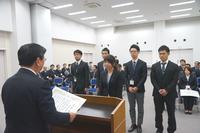 演台で賞状を読み上げる男性の前に1人の女性が立ち、その後ろに4名の男性が立っている写真