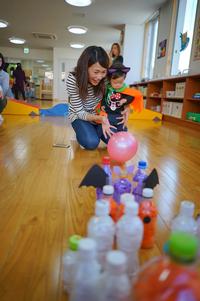 室内で、仮装した子どもと大人がペットボトルを使ったボウリング遊びを楽しんでいる様子の写真