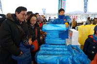 青い袋に詰められた品物を、人々が手に取りながら並ぶ市場の写真