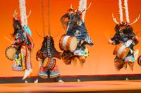 色鮮やかな伝統衣装に身を包み、頭に長い飾りをつけた踊り手たちが腰に太鼓をつけて力強く跳び上がりながら演奏している迫力ある郷土芸能の舞台の写真