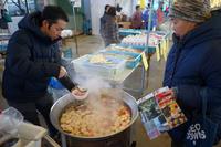 白い器に大鍋から湯気を上げたおでんを盛り付ける男性と、それを見つめる来場者の写真