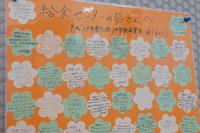 オレンジ色の台紙に白と緑の花の形をした用紙がたくさん貼られ、それぞれに「給食センターの皆さんへ」と題して子どもたちからの感謝のメッセージが手書きで書かれている掲示物の写真