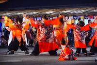オレンジ色の法被を着た集団が、両手と両足を広げて力強い動きで演舞を披露している様子の写真