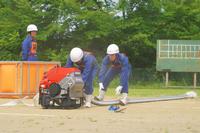 2人の団員がポンプとホースを接続している様子を横から捉えた訓練中の写真