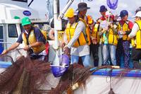 黄色のライフジャケットを着た参加者の1人が2匹の魚を定置網からタモですくった写真