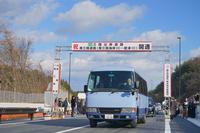 青空の下、新しく開通した高速道路のゲートを青いマイクロバスが通過している写真