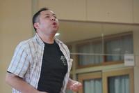 チェック柄のシャツを着た男性が真剣な表情で口をすぼめてスイカの種を飛ばしている瞬間の写真