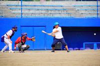 水色のヘルメットをかぶった男性が白いTシャツ姿で打席に立ち、ボールにバットを合わせようとしている様子の写真