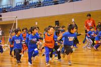 多くの子どもたちが青やオレンジの服を着て体育館を元気に走っている様子の写真