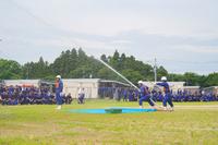 水が勢いよく噴き出すホースを3人の団員が操作している、放水訓練中の写真