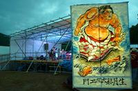 力士の大きなイラストが描かれた立て看板の後ろで、夕方のステージ演奏が行われている写真