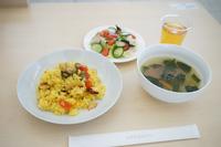 黄色く色づけされたパエリアのようなご飯、スープ、サラダが配膳されている写真