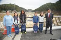 5名の女子小学生が「新井田橋」と書かれた橋名板が設置された橋の上で記念撮影をしている写真