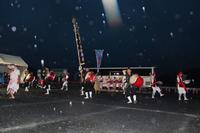 雨が降る中、夜のイベントで和太鼓の演奏をする人たちが隊列を組んでエイサーを踊っている写真