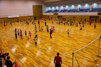 体育館全体を上から見た構図で、広いフロアでたくさんの子どもたちがサッカーをしている様子の写真