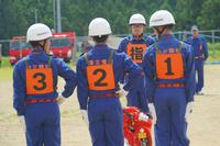 「1番」「2番」「3番」と背中に書かれたビブスを着た団員が指示を受けて整列している写真