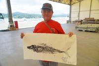 魚拓をとった紙を両手で持ちカメラに見せている男の子の写真