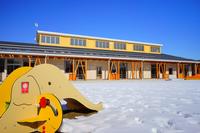 幼稚園の園庭に面した明るい黄色の外壁の園舎と、手前に象の形をした遊具がある様子の写真