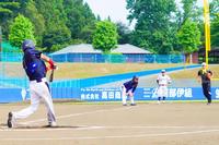 青いヘルメットをかぶった野球選手がバットを振り、打球が飛んでいく瞬間を捉えたグラウンド上の様子の写真