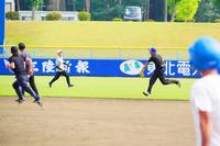 黒い服を着た数名の人たちが野球場の外野を全力で走っている写真