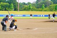 白いユニフォームの打者が構え、黒いユニフォームの投手がボールを投げる瞬間の試合風景の写真