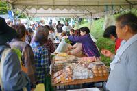 テントの下で地元の人々が卵や干物、惣菜などを販売し、買い物客でにぎわっている様子を写した写真