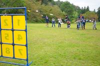 芝生の上で子どもたちがフリスビーを黄色の的に向かって投げるゲームに挑戦している様子の写真