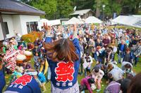 法被姿の女性が前方に向かって何かを撒いており、それを受け取ろうとたくさんの人が手を伸ばしているにぎやかな祭りの様子を写した写真