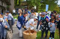 割烹着を着た女性と法被姿の男性が木製のうすと杵で餅をつき、その周りで大勢の人や子どもたちが楽しそうに見守っている餅つき大会の写真