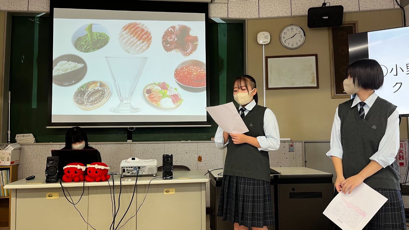 スクリーンには、海産物やご飯、ガラスの器などの写真が表示されており、高校生2人がプレゼンテーションをしている様子の写真
