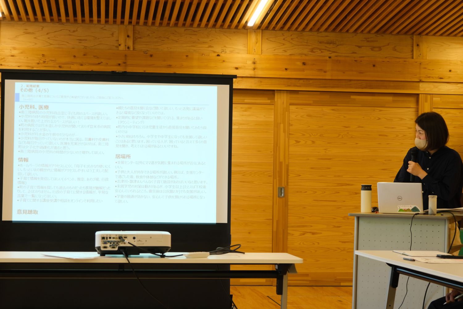 マスクを着けた栗林さんがマイクを持ち、ノートパソコンを使いながらスクリーンに映った資料を説明している写真